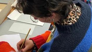 Student writing on paper whilst reading a book in the university archives