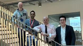Four people standing in a row on a staircase, smiling