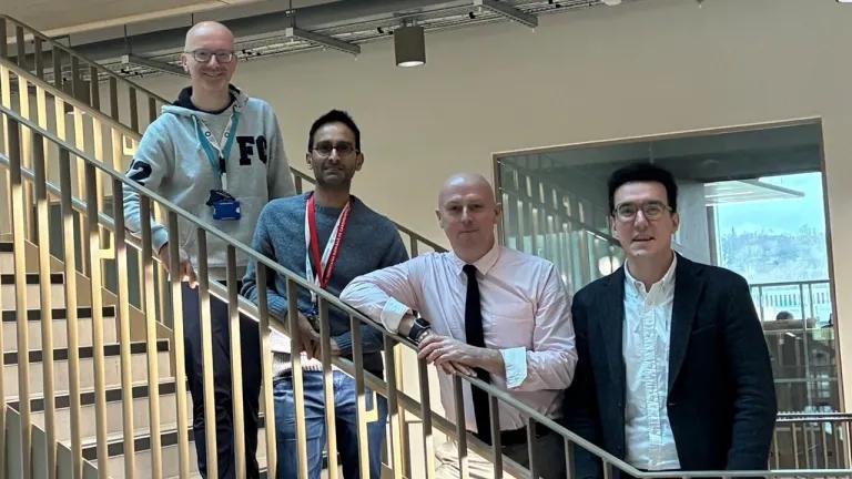 Four people standing in a row on a staircase, smiling
