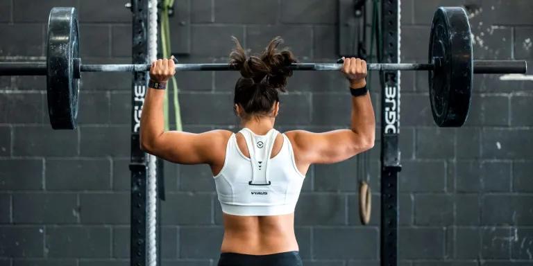 woman lifting wights overhead at the gym flaxing back muscles 