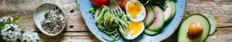 Blue bowl of green vegetables and boiled eggs sitting on a wooden table 