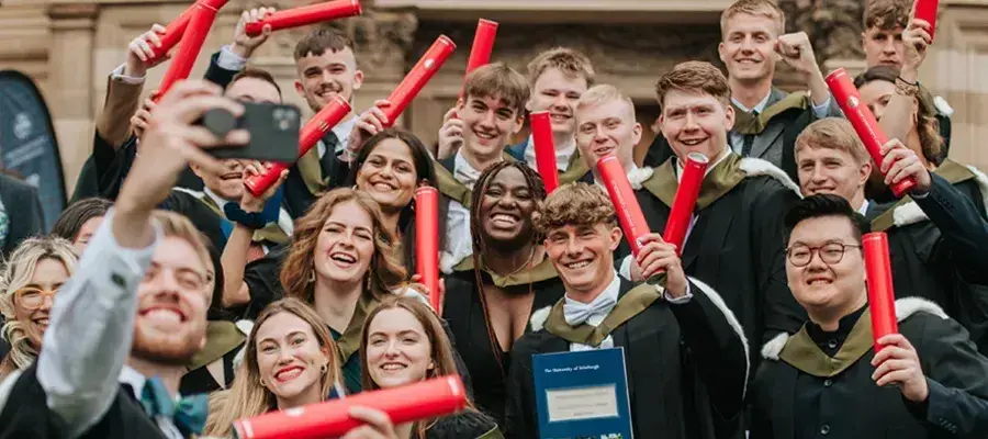 A group of happy graduates in robes holding up their certificates