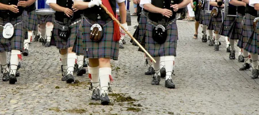 Cropped image showing people in kilts marching along a cobbled street.