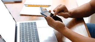 Someone using a mobile with laptop in background