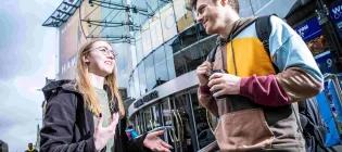 Two students talking outside a university building with a glass front