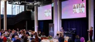 Shot of crowd at staff awards event with plasma screen displays in background
