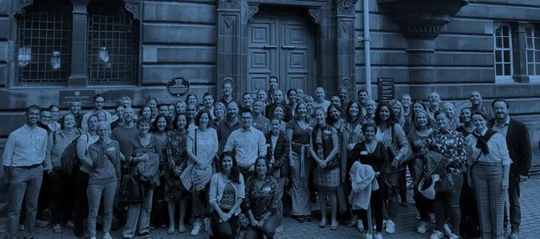 Class photo of an alumni group outside a door at the Old Medical School.