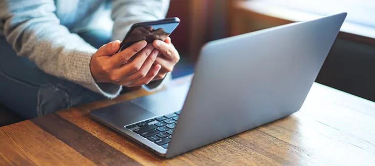 woman sitting holding a phone next to an open laptop