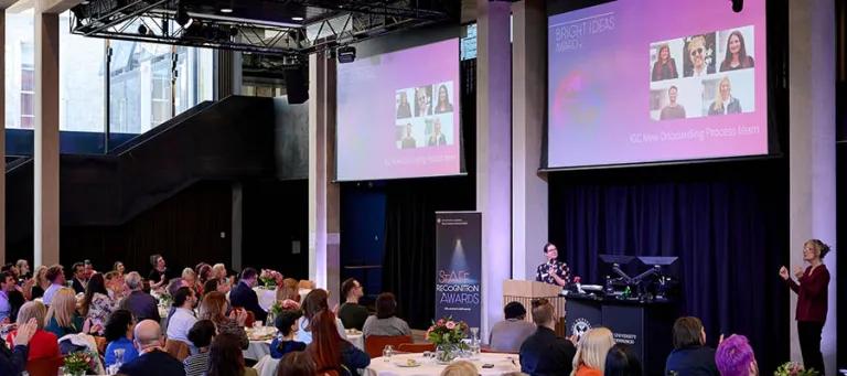 Shot of crowd at staff awards event with plasma screen displays in background
