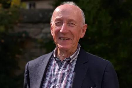 John Gillies, smiling, wearing a suit while standing outside