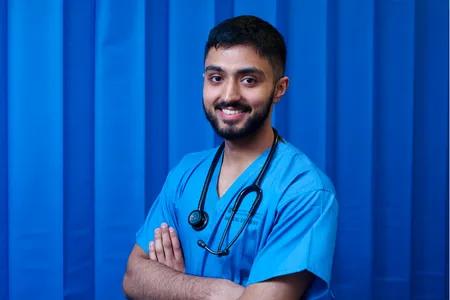 Mid shot of Suleman in scrubs against blue backdrop