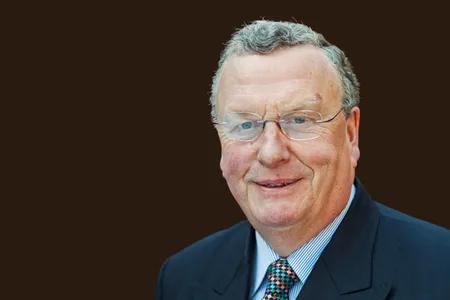 Nairn Wilson, smiling, wearing a suit and glasses