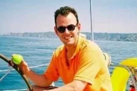 Robin, wearing sunglasses, at the helm of a boat on the ocean