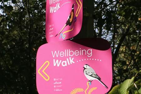 A sign in the foreground reading "Wellbeing walk" with trees in the background