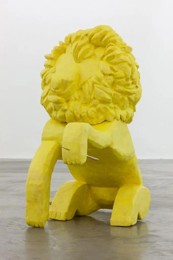 This picture represents a sculpture made by Isabel Nolan in 2015, entitled "A lion with a thorn in his paw". The scripture is a bright yellow lion sat on its hind legs, raising its left front paw pierced by a thin thorn. The sculpture is made out of polystyrene, plaster bandage, and papier mâché. It measures 109 by 59 by 118cm.