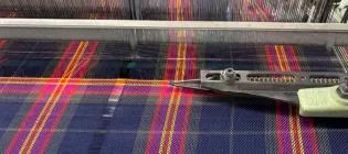 Image of tartan being produced in the mill will a tool on the material