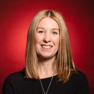 portait of woman smiling with strawberry blonde hair wearing a black top with dark red background