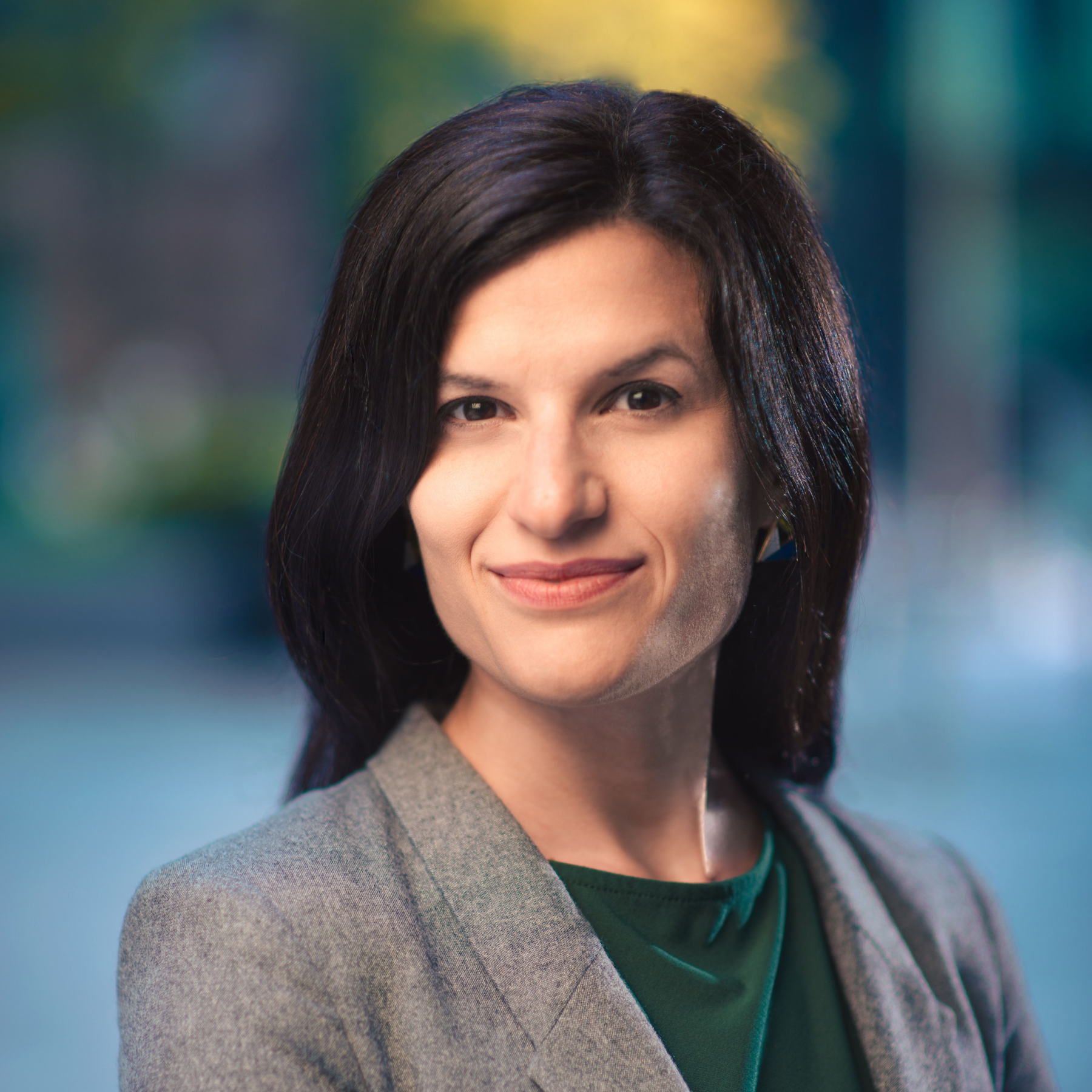 portait of woman smiling with no teeth, short dark hair, wearing a grey blazer and green top