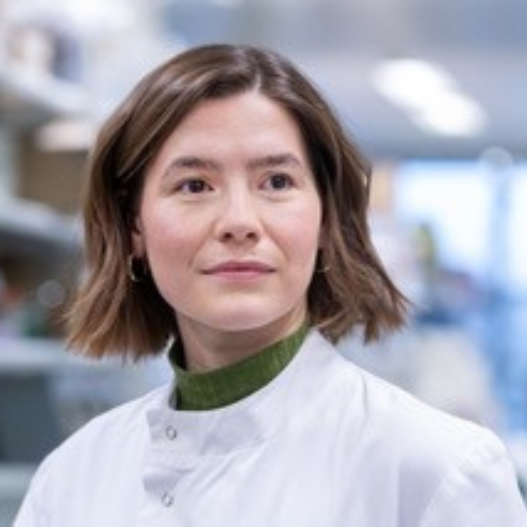 Portait of woman in a lab setting, with short brown hair and a lab coat