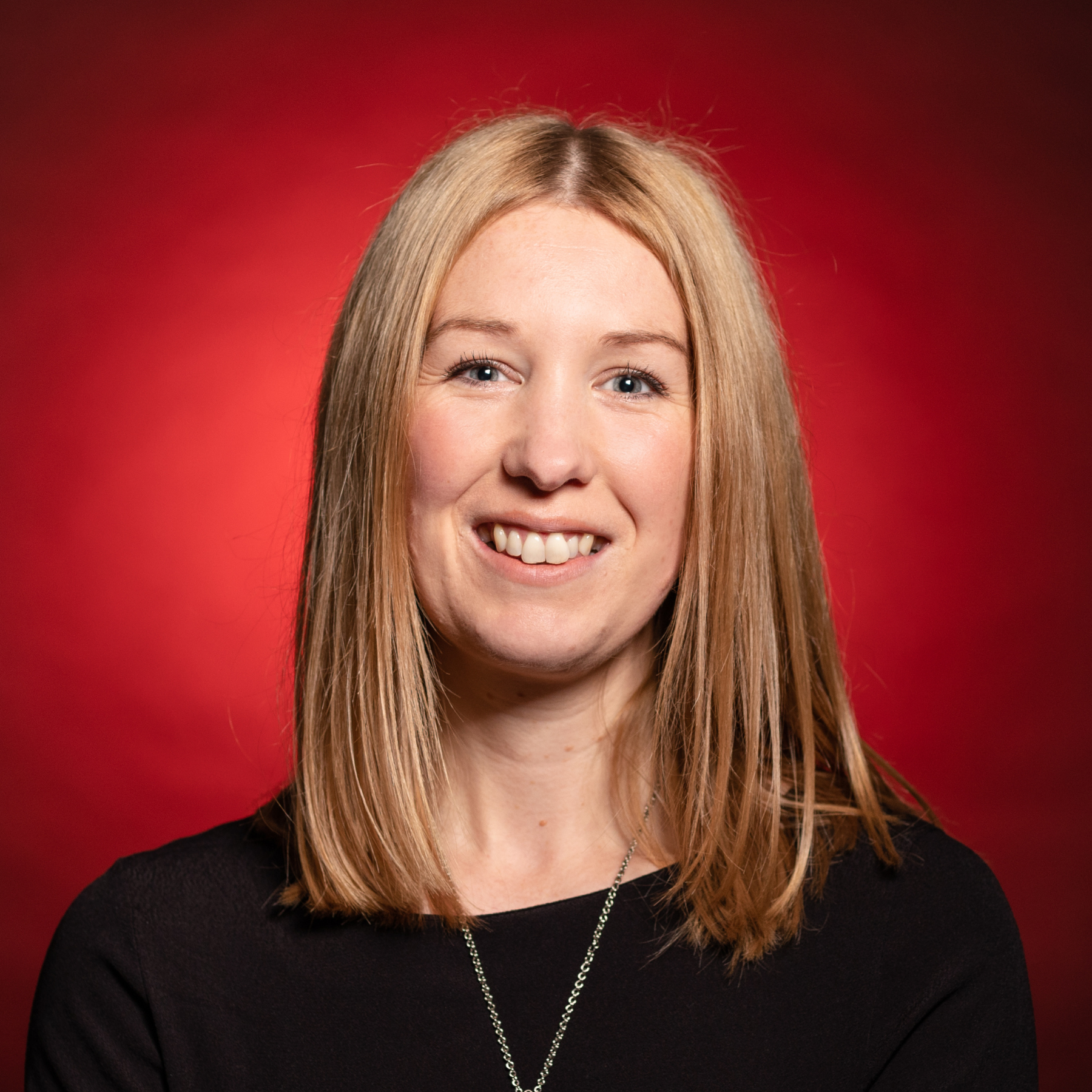 portait of woman smiling with strawberry blonde hair wearing a black top with dark red background