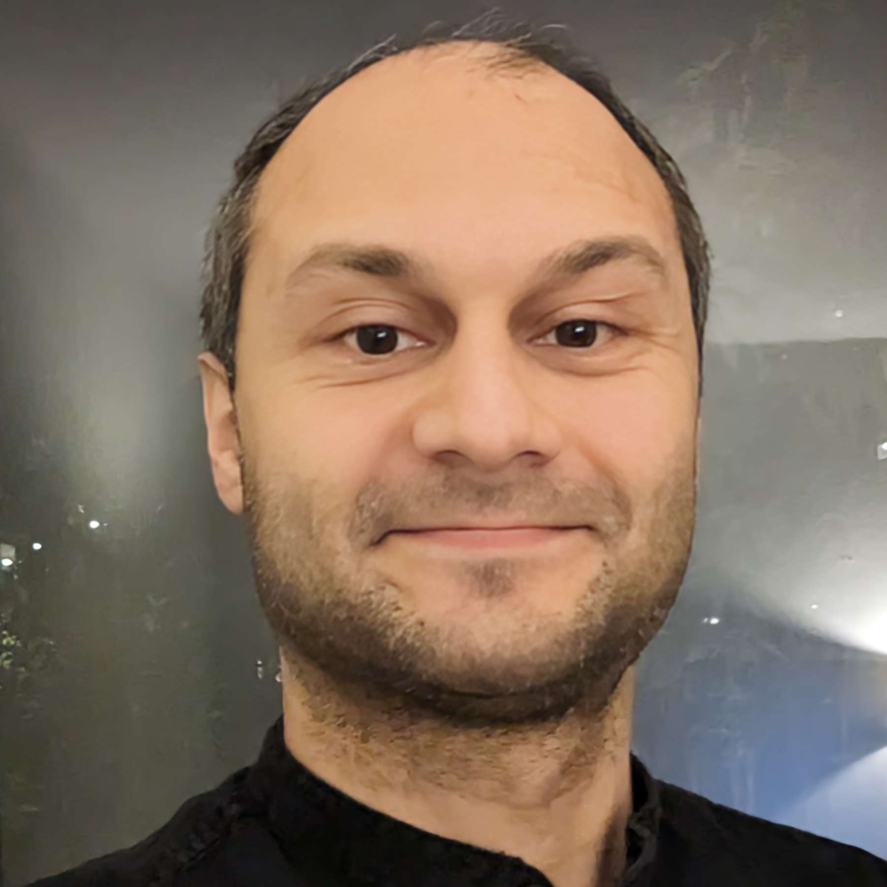 portair of man with dark hair and beard smiling, with a plain background